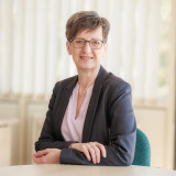 Frau mit Anzugjacke und rosa Bluse am Schreibtisch