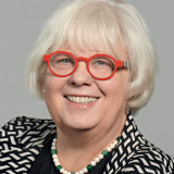 Porträt blonde Frau mit roter Brille und schwarz-weiß gemustertem Jacket