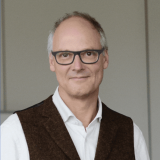 Porträt eines Mannes mit Brille, weißem Hemd und Weste